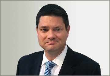 A headshot of Peter Corcoran Esq., a man in a suit and patterned tie, with