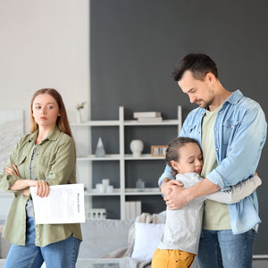 Man hugs child, woman holds papers looking upset. Implies child custody discussion.