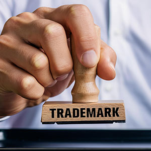 Hand stamping TRADEMARK on a document, illustrating brand protection and intellectual property law.
