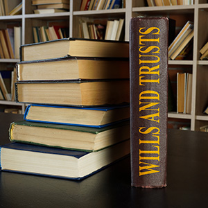 Stack of law books with one titled Wills and Trusts standing upright in a library background.